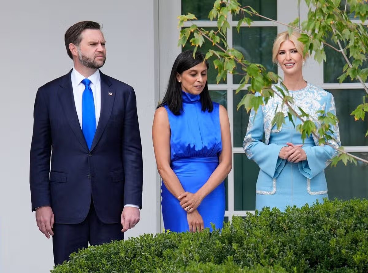 Tres personas juntas en un ambiente formal, probablemente afuera de un edificio oficial. Están vestidos con traje formal; el de la izquierda tiene un traje oscuro, el del medio es azul y el de la derecha es azul claro. Estaban junto a un seto y una ventana con marco blanco.