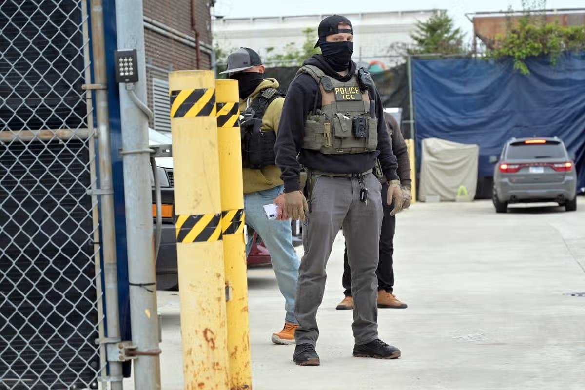 Oficiales del Servicio de Inmigración y Control de Aduanas (ICE) con chalecos tácticos y máscaras hacen guardia dentro de la puerta perimetral de una instalación de procesamiento de ICE en Beach Street mientras los manifestantes se reúnen afuera para una manifestación de aniversario para conmemorar el primer aniversario de las protestas de Midway Blitz en Broadview, Illinois, Estados Unidos, el 25 de septiembre de 2026.