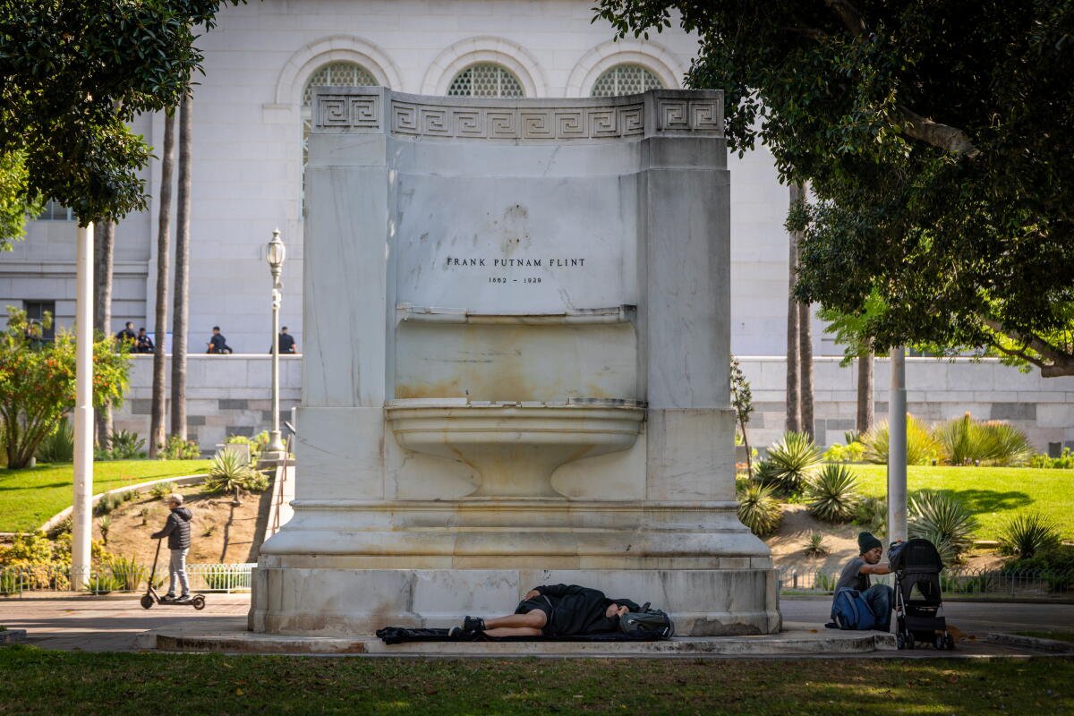 La gente duerme y descansa en una fuente a la sombra frente al Ayuntamiento