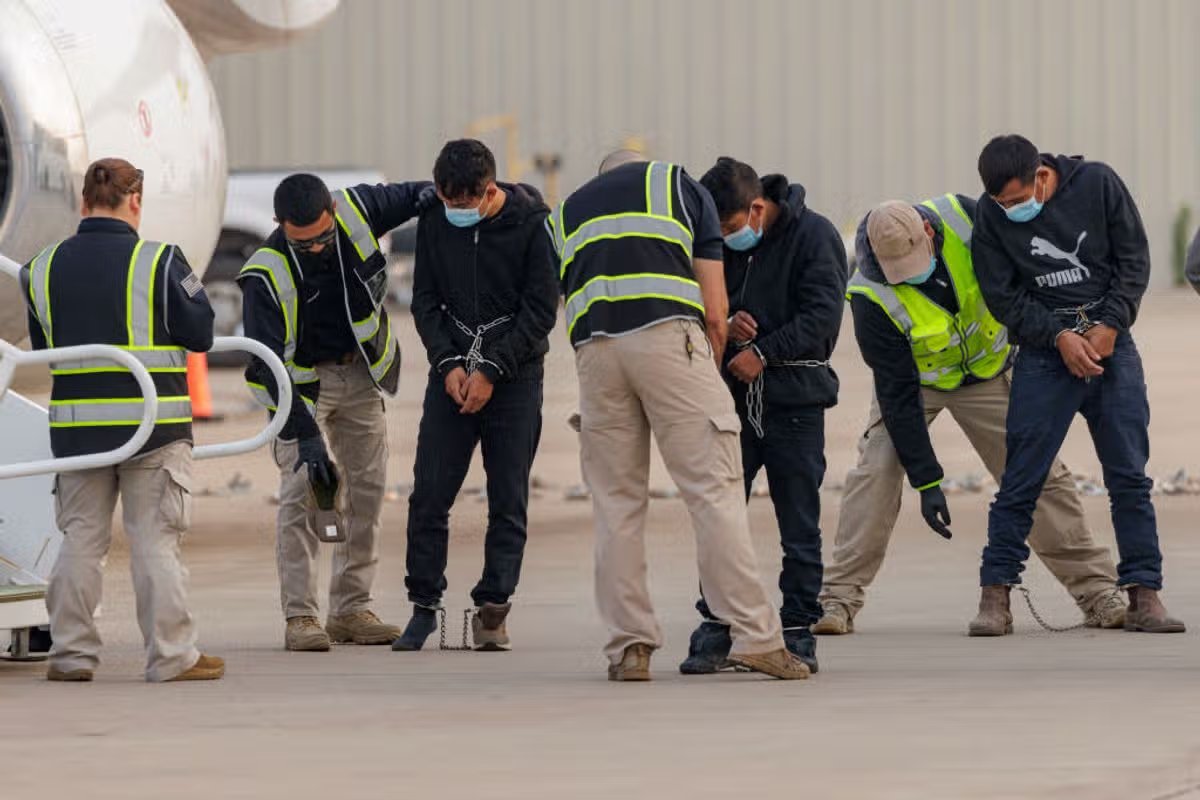 Agentes de seguridad registran a inmigrantes encadenados detenidos por ICE antes de abordar un avión con destino a Guatemala.