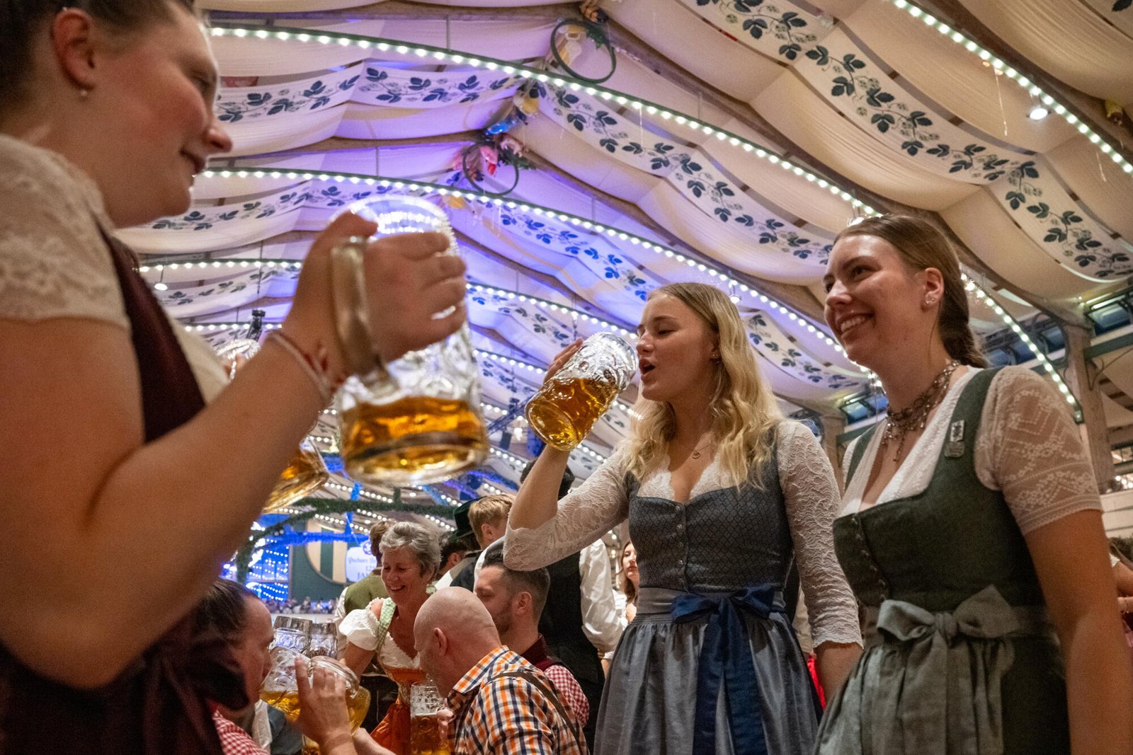 Tres mujeres se paran en los bancos del Pschorr Braurosl Festzelt y beben cerveza.