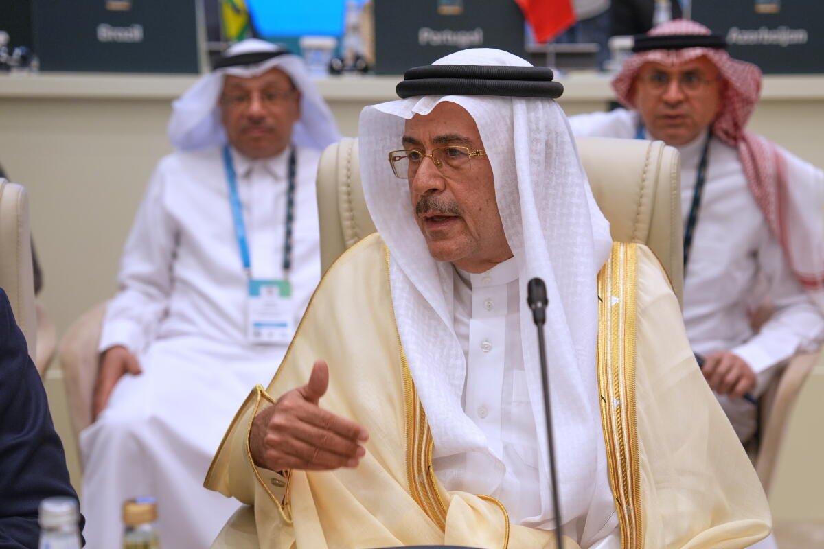 Un hombre saudita bien vestido se sienta con otros. Está hablando con un micrófono frente a él. 