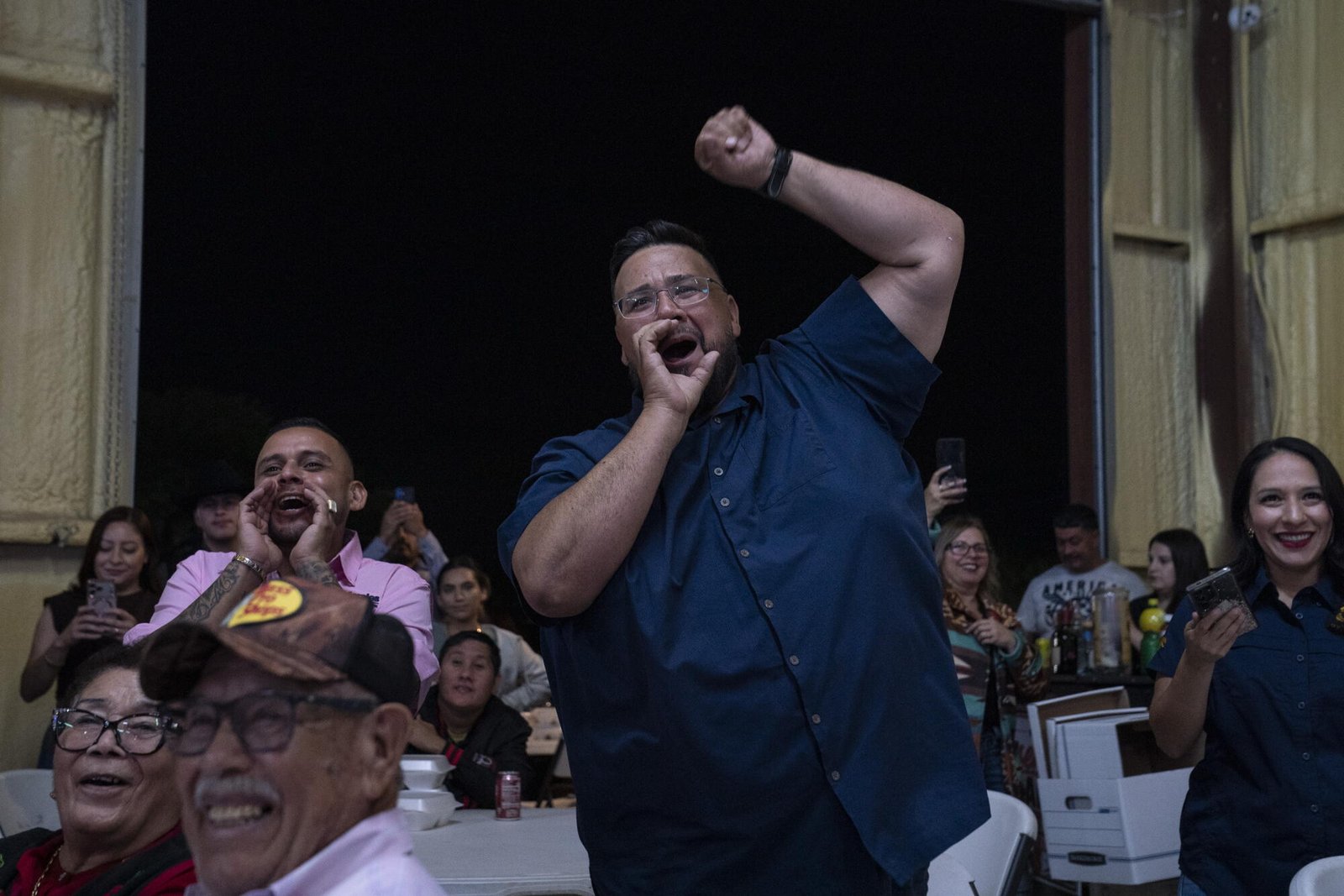 La gente aplaude cuando un hombre vestido con una camisa oscura de manga corta levanta el puño mientras habla en un mitin.