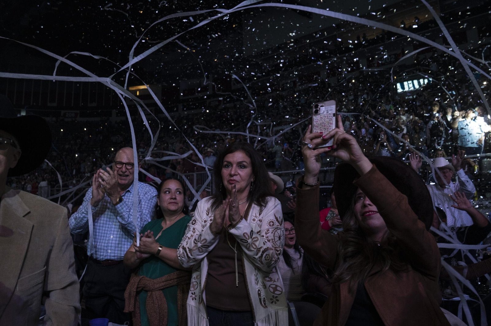 La gente aplaude mientras algunos toman fotos con sus teléfonos móviles mientras ondean pancartas en un concierto.