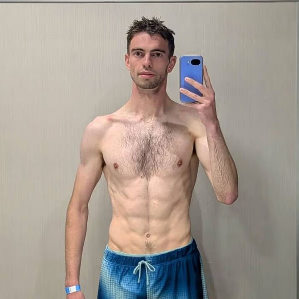 Un hombre de pelo corto se toma un selfie con un teléfono móvil azul en el baño.